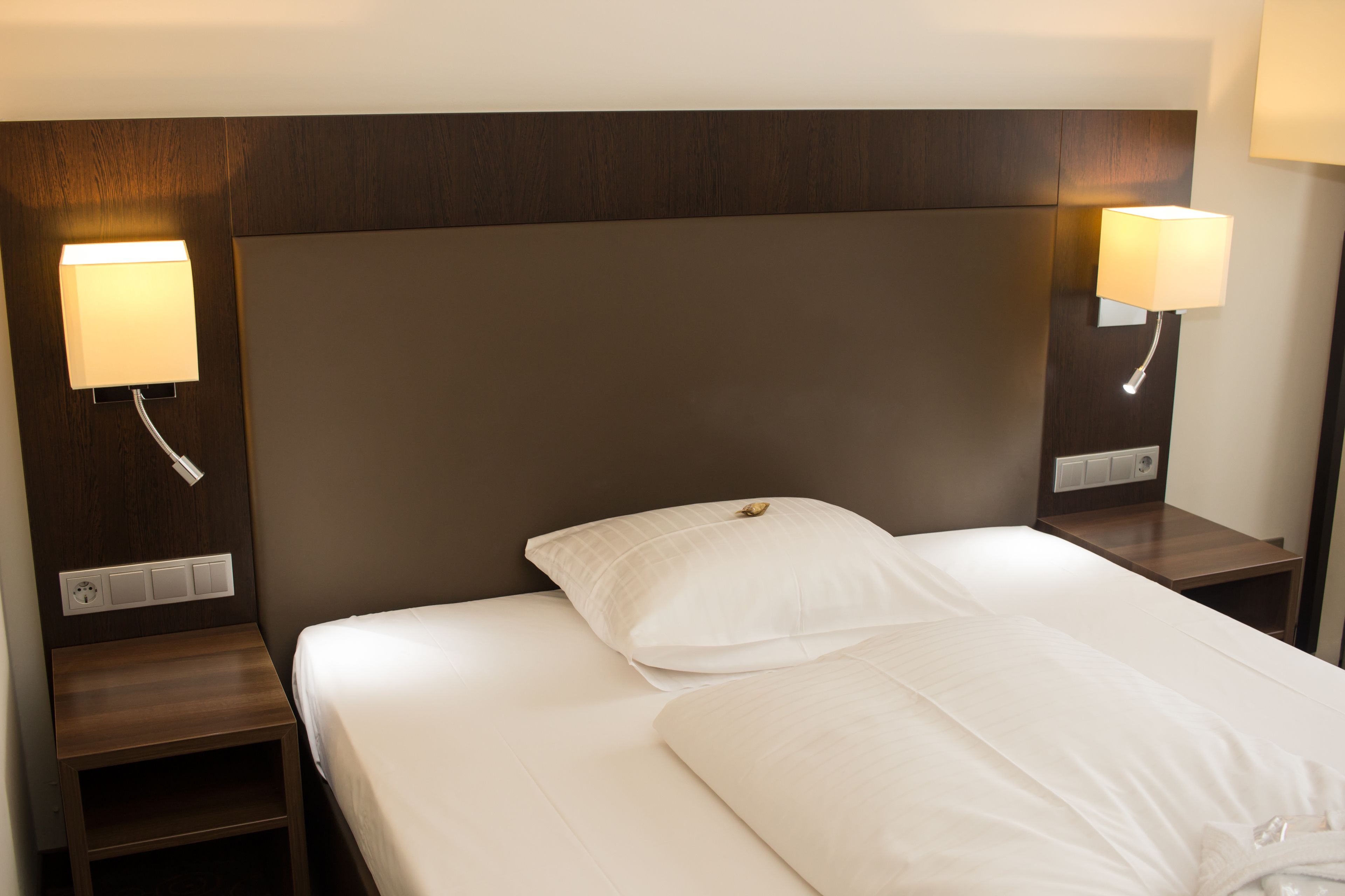 A neatly made bed with white linens and two bedside lamps on wooden nightstands.