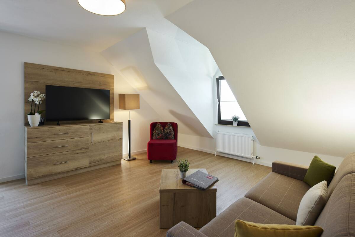 A modern living room with a flat-screen TV, a red chair, a brown sofa, and a wooden coffee table.