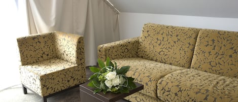 Una habitación con un sofá y un sillón de estampado floral, una pequeña mesita de madera con un arreglo floral, y una alfombra estampada.