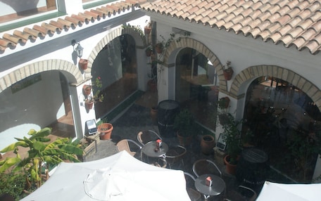 An outdoor patio area with multiple tables and chairs, surrounded by potted plants and a tiled roof.