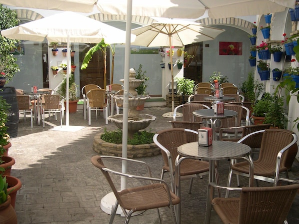 Un espace extérieur aménagé en terrasse, avec des chaises et des tables en osier, des parasols et des plantes en pot.