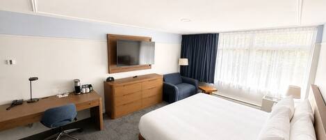 Habitación de hotel con cama, escritorio con silla, cómoda, televisor, lámpara y ventana con cortinas.