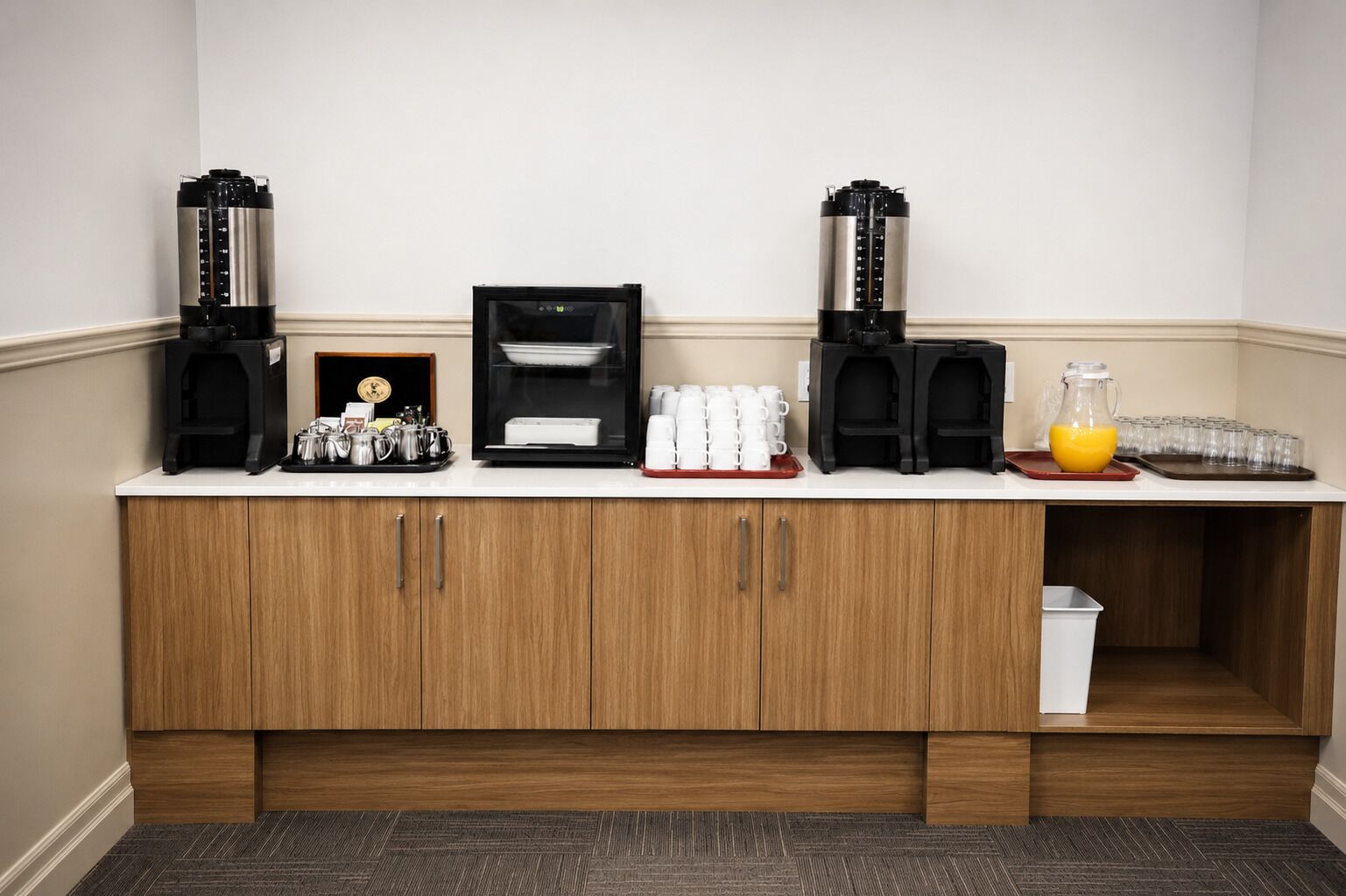 A kitchenette with coffee makers, a coffee machine, a juice pitcher, and a tray of cups.