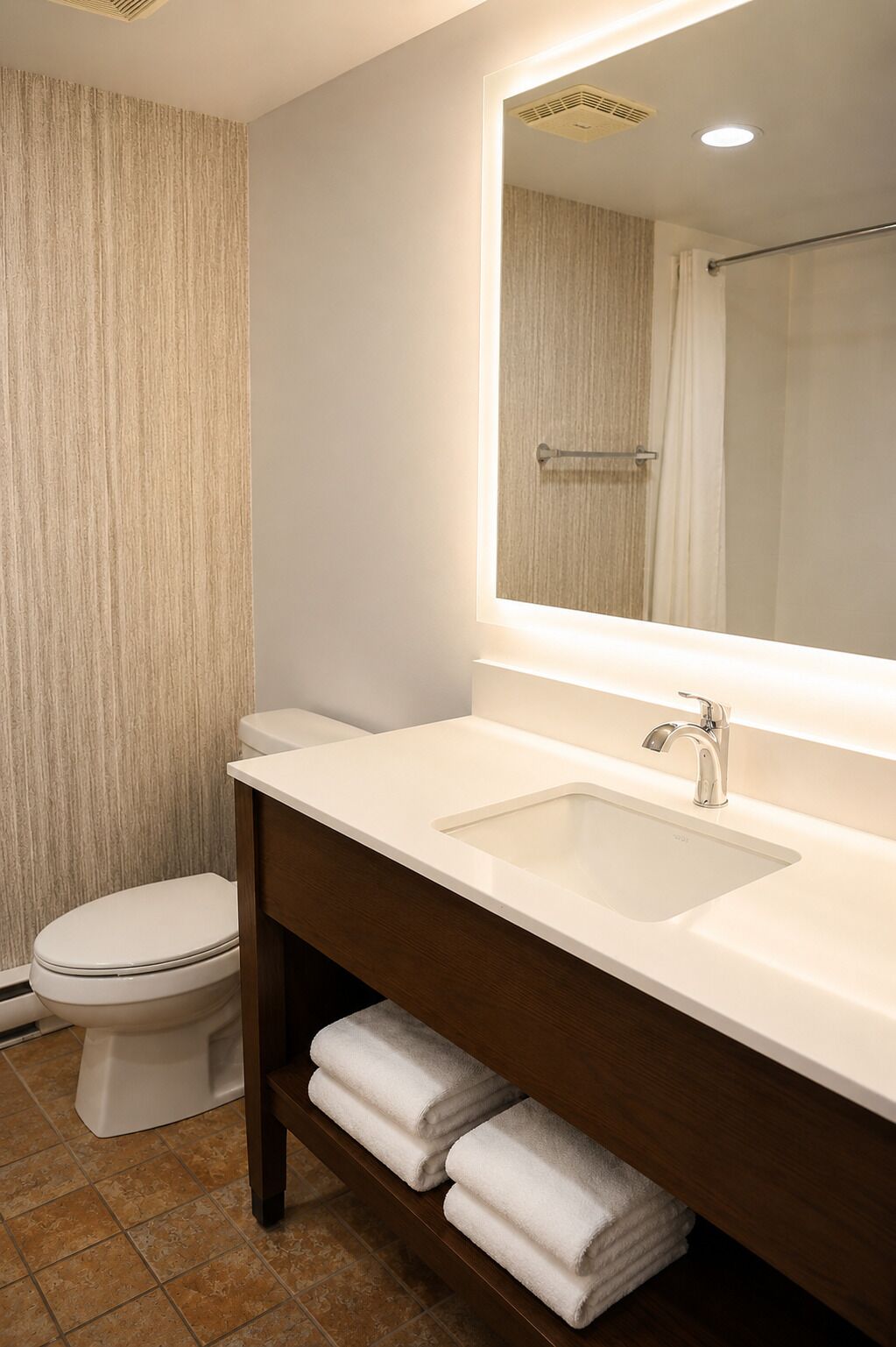 A bathroom with a toilet, sink, mirror, and towels.