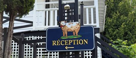 A reception sign with a goat illustration and a directional arrow, mounted on a porch with a stone wall and wooden fence.