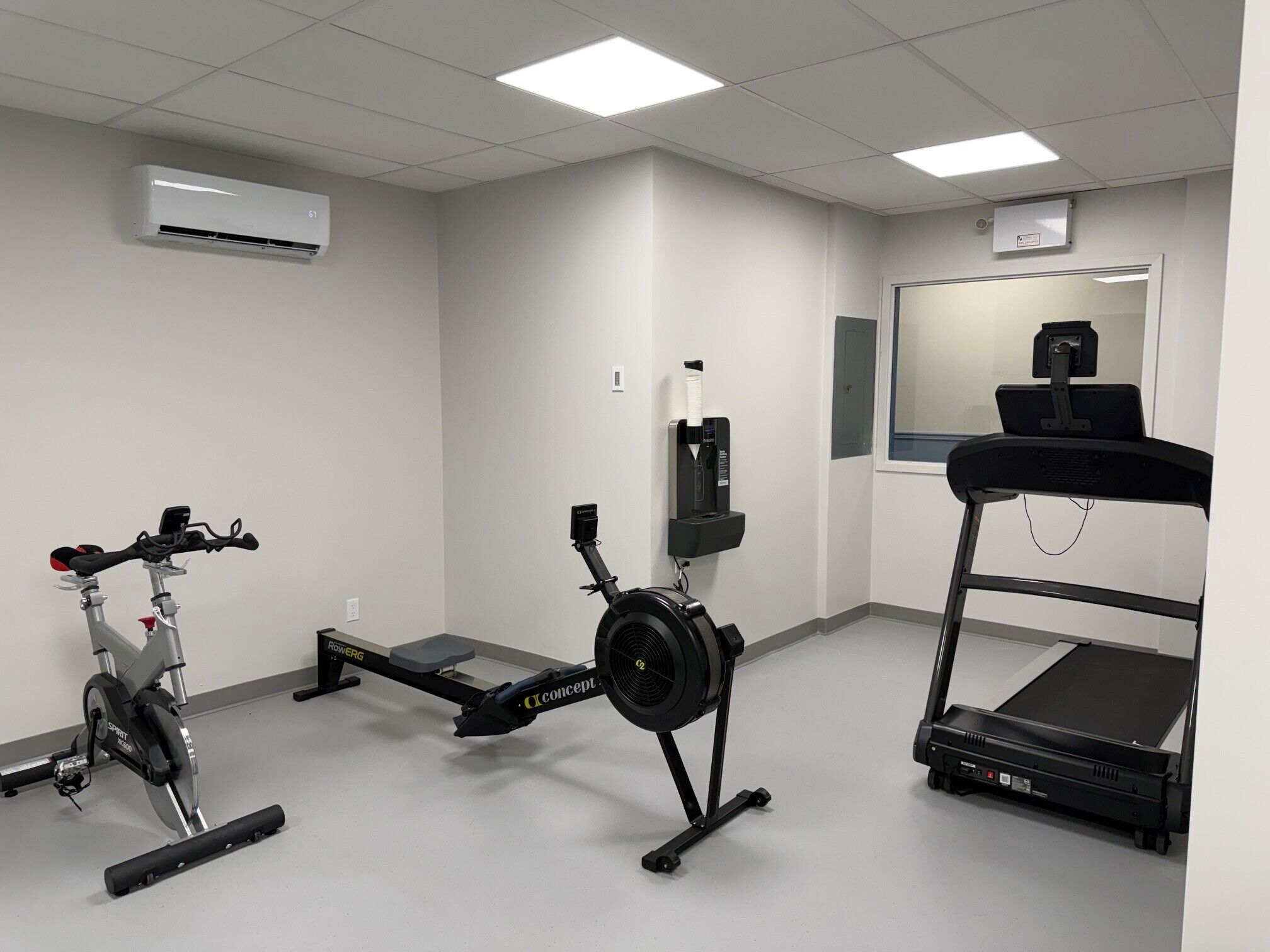 A fitness room with a stationary bike, a rowing machine, a treadmill, and a mirror.