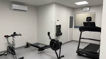 A fitness room with a stationary bike, a rowing machine, a treadmill, and a mirror.
