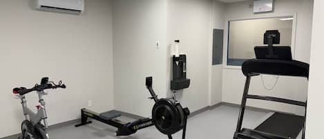 Gimnasio con bicicleta estática, máquina de remo, cinta de correr y un espejo.