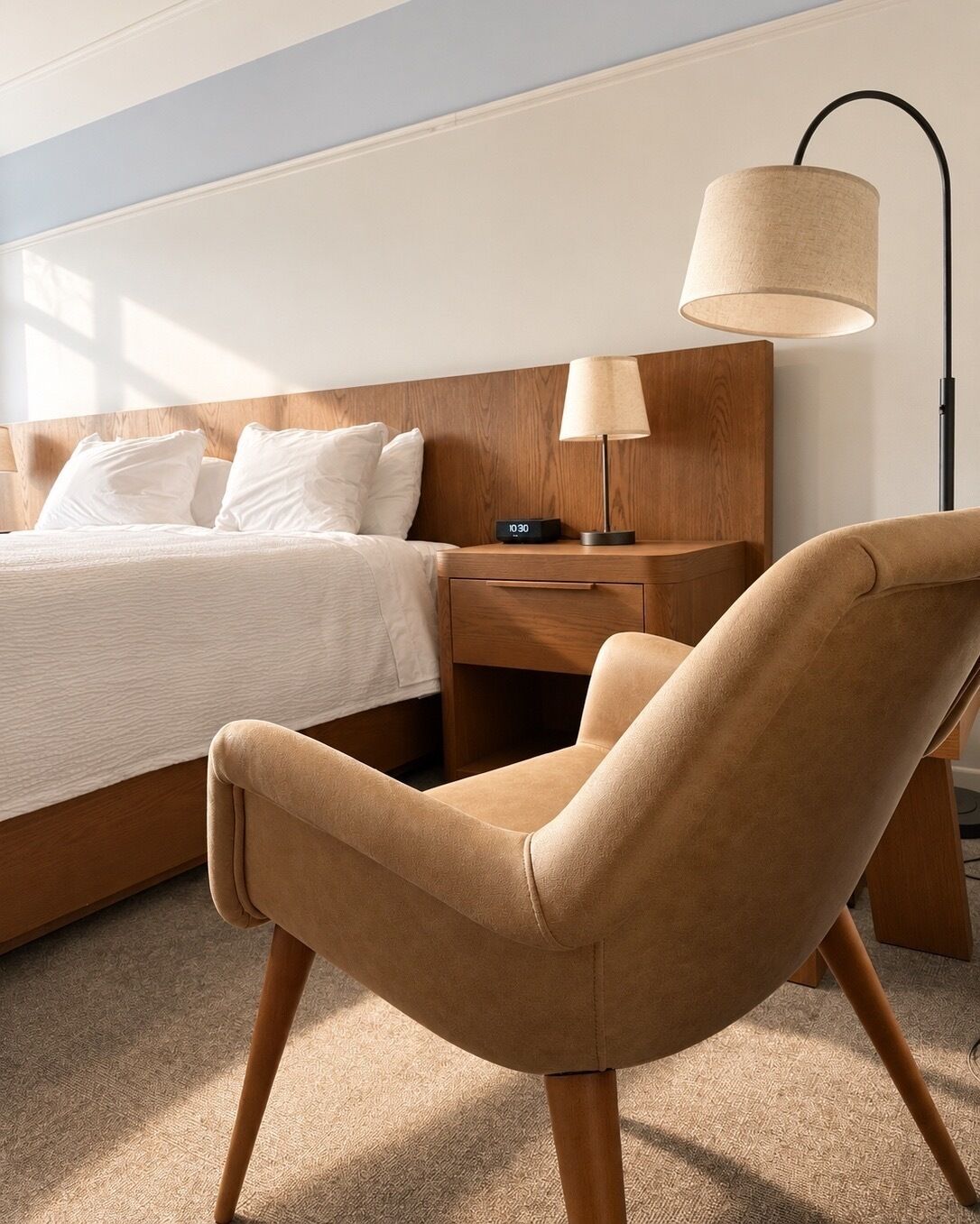 Een hotelkamer met een bed, nachtkastje, lamp en stoel.