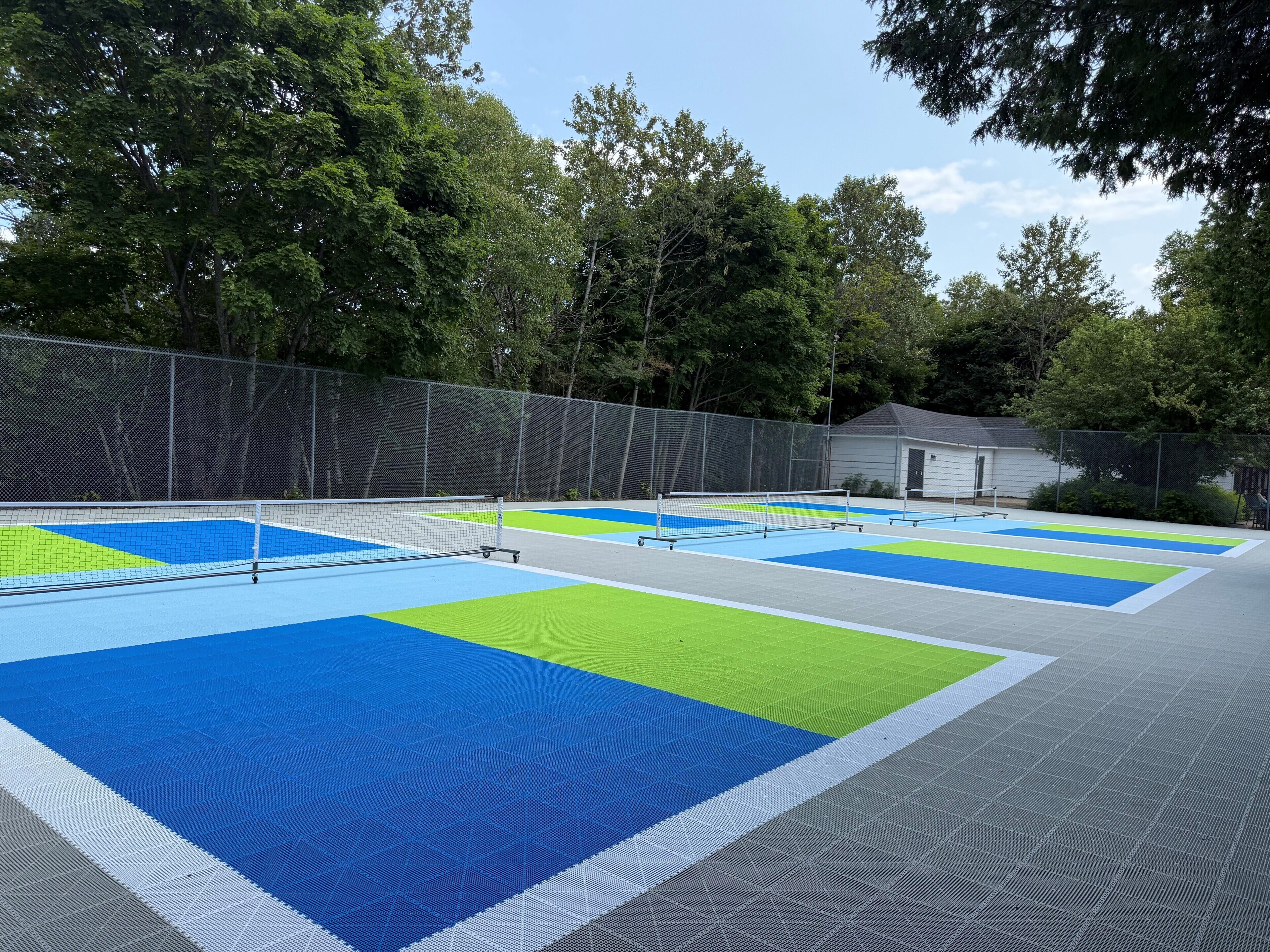 An outdoor tennis court with a net, surrounded by trees and a fence.