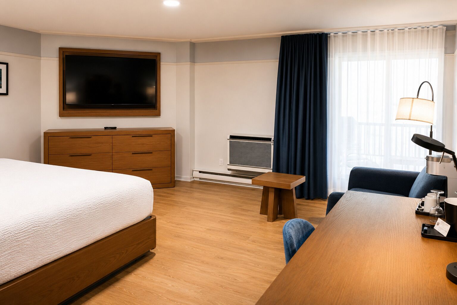 A hotel room with a bed, a desk, a chair, a TV, a heater, and a window with curtains.