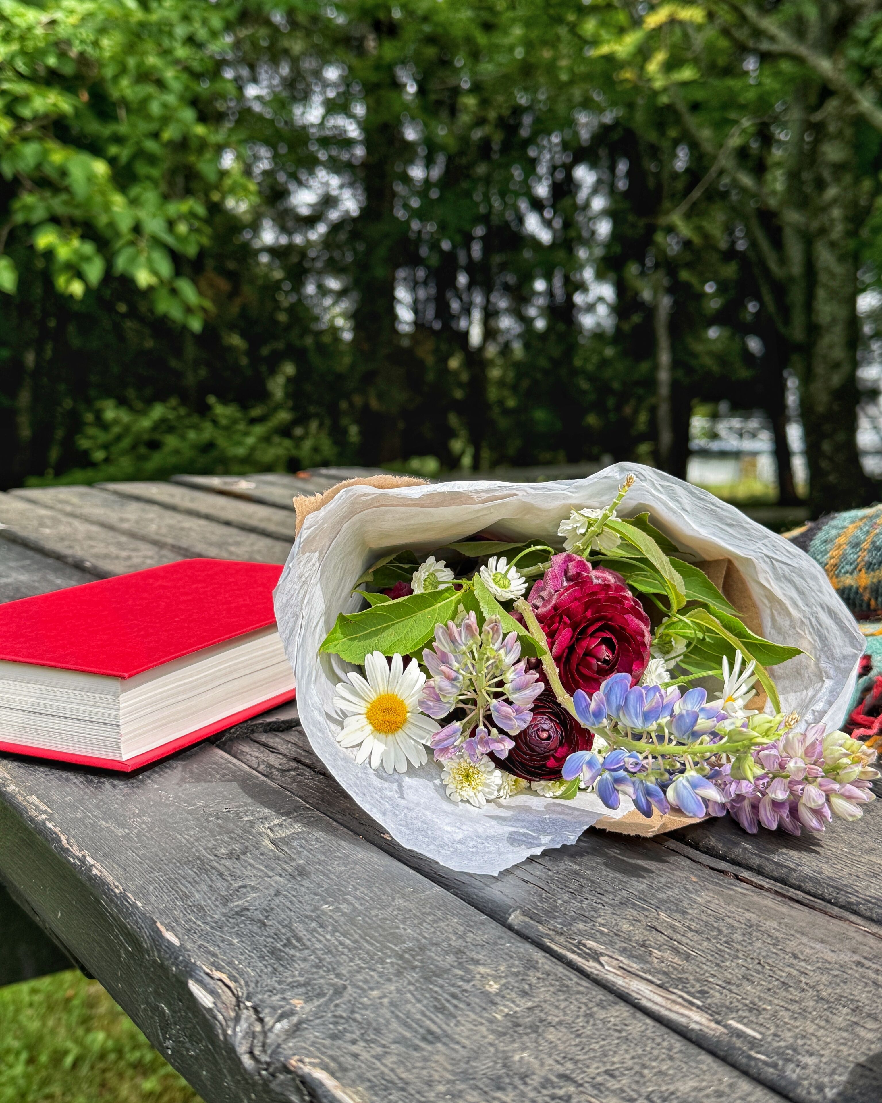 Ein Picknicktisch mit einem roten Buch und einem Blumenstrauß.