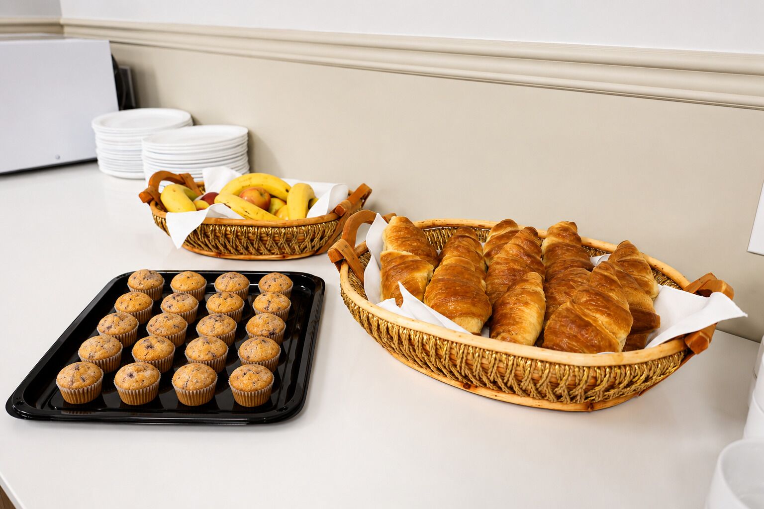 Une table de buffet avec des muffins, des croissants et des fruits.