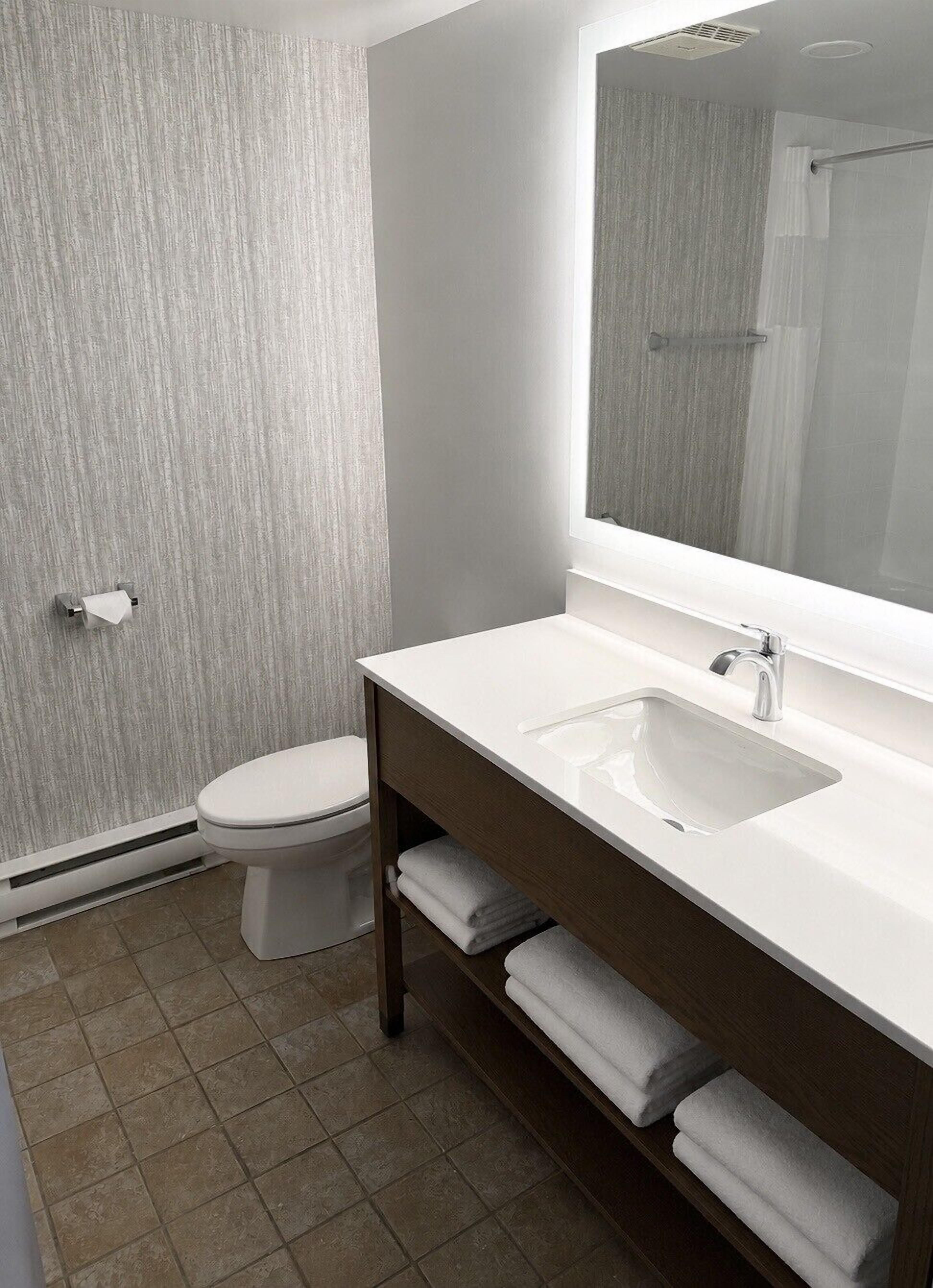 Un baño con inodoro, lavamanos con espejo y toallero.