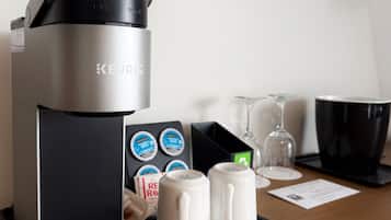 Una cafetera Keurig con una bandeja, dos tazas blancas y una caja de cápsulas Adagio sobre una mesa de madera.