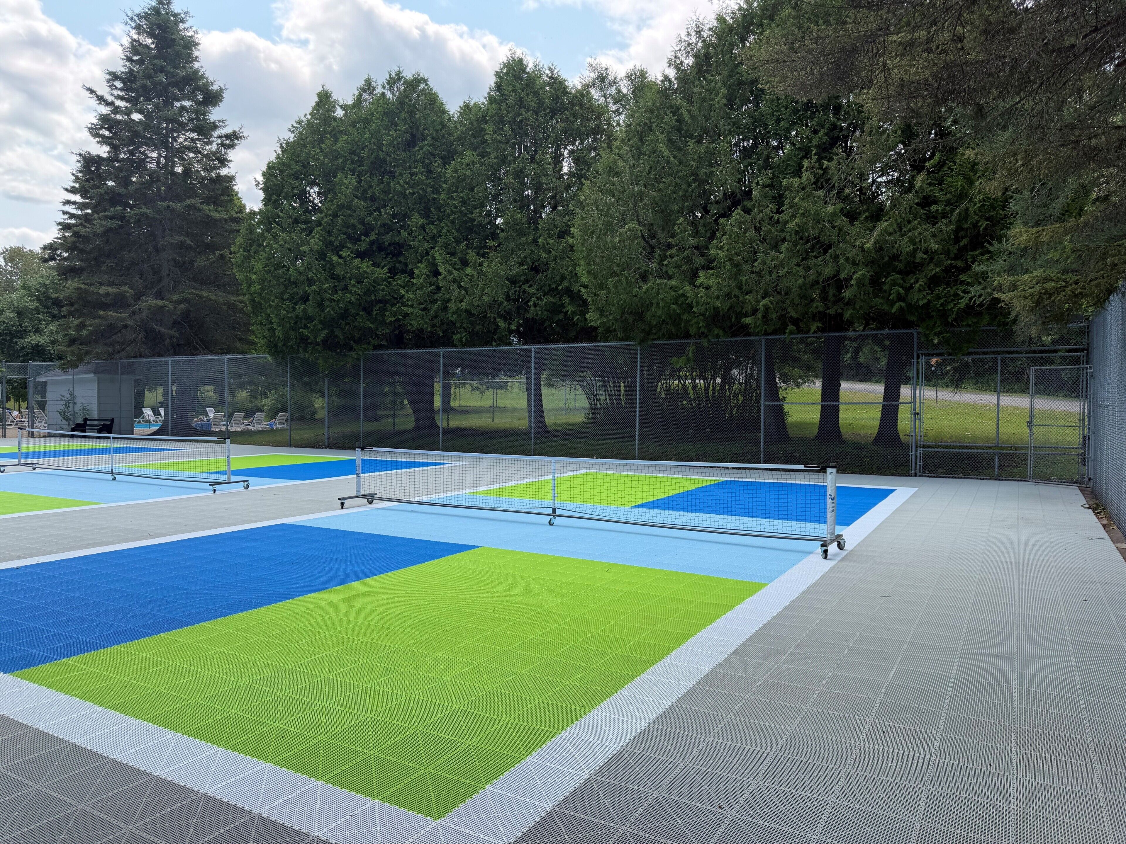 Cancha de tenis exterior con red, rodeada de árboles y una valla.