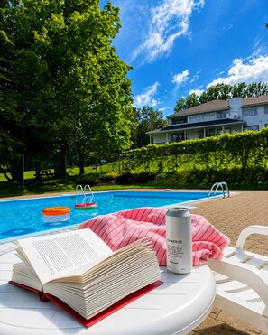 Escena junto a la piscina con un libro, una lata y una toalla rosa sobre una silla de descanso blanca.