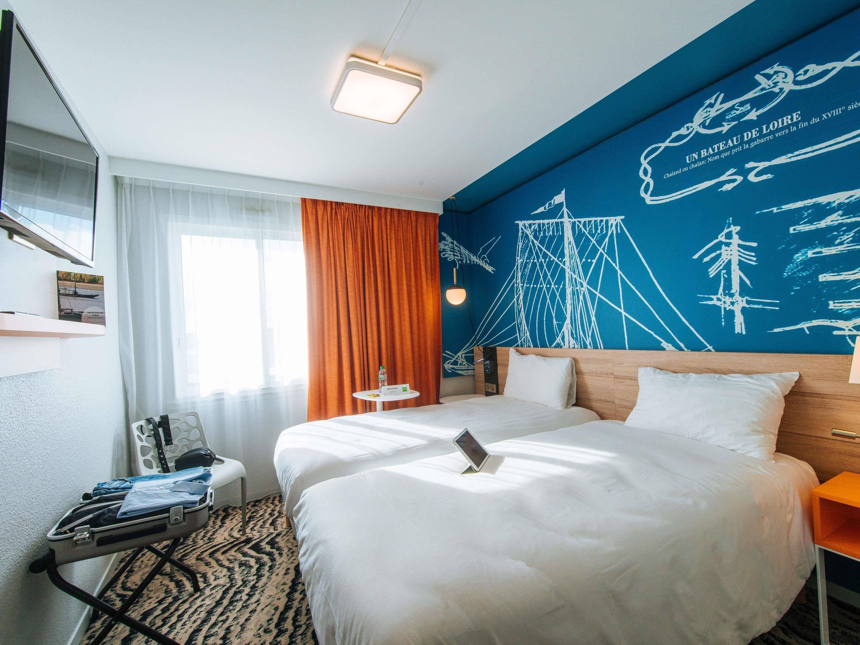 Habitación de hotel con dos camas, un escritorio, una silla, una mesita y una pared decorada con motivos náuticos.