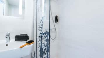 Une salle de bain avec un lavabo blanc, une douchette à main et un sac noir posé sur le comptoir.