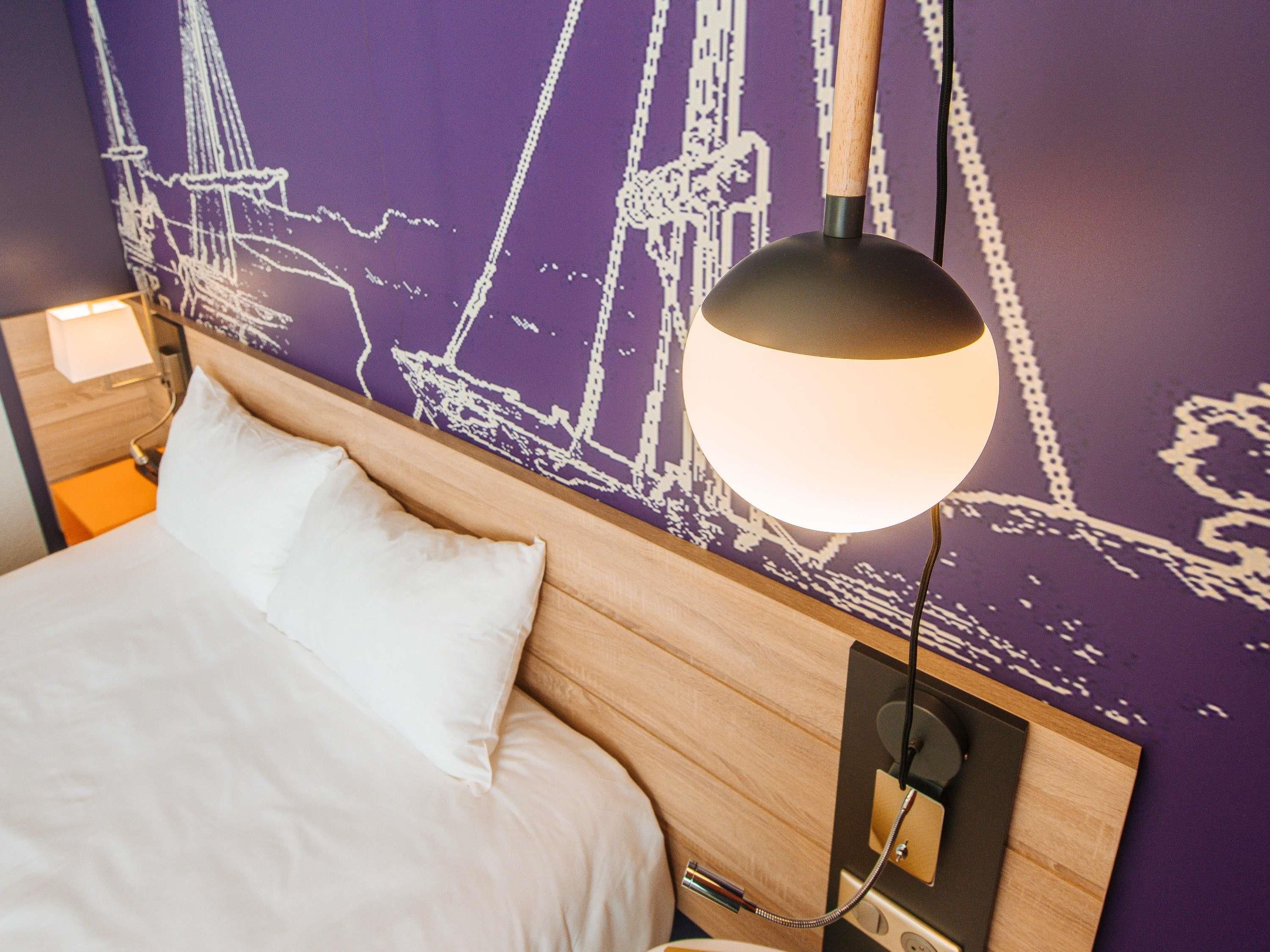 A hotel room with a bed, a nightstand, a lamp, and a wall with a nautical-themed mural.