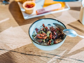 A bowl of granola with seeds and dried fruits on a wooden table.