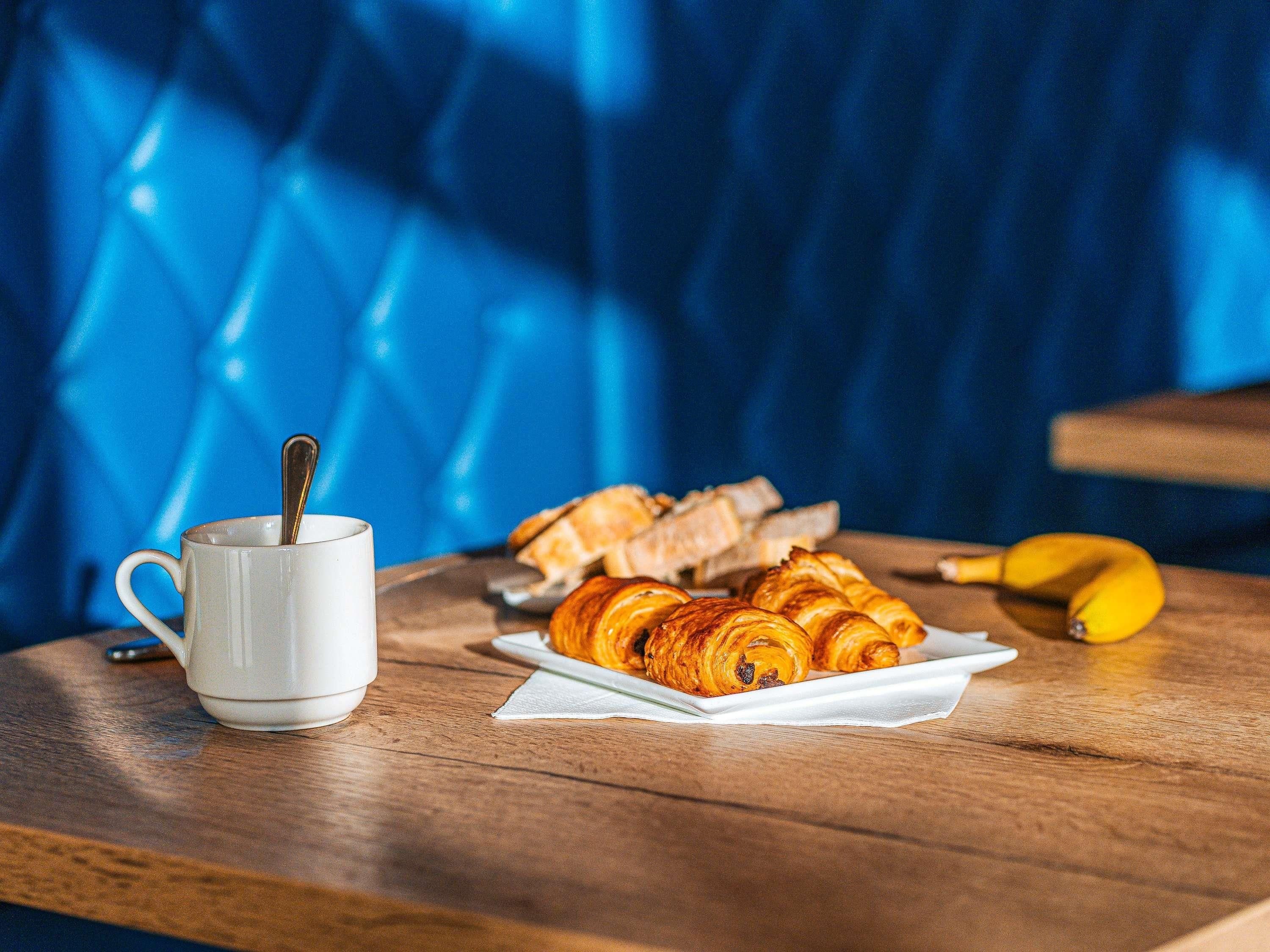 A wooden table with a white mug, a banana, and pastries.