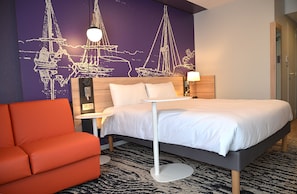 Ein Hotelzimmer mit Bett, Nachttisch, Lampe, Stuhl und einer Wandmalerei mit Segelbooten.