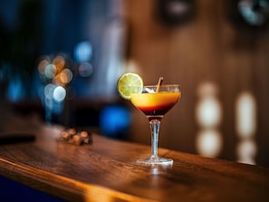 A cocktail in a glass with a lime garnish on a wooden bar counter.