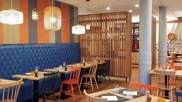 Restaurante com assentos em cabines forradas de azul, mesas de madeira e cadeiras laranja.