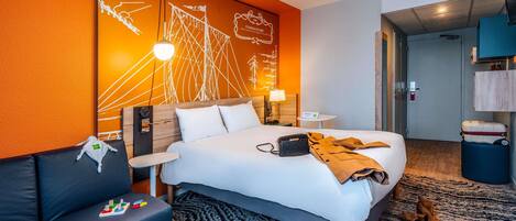 Habitación de hotel con cama, sofá de cuero negro, una mesita y una pared decorada con un mural.