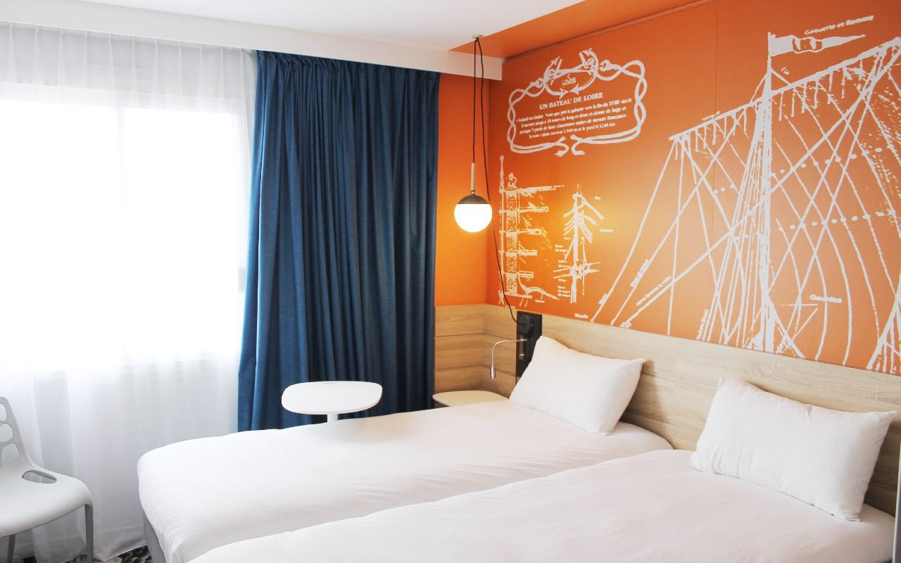 A hotel room with a large bed, a small table, and a wall with a map design.