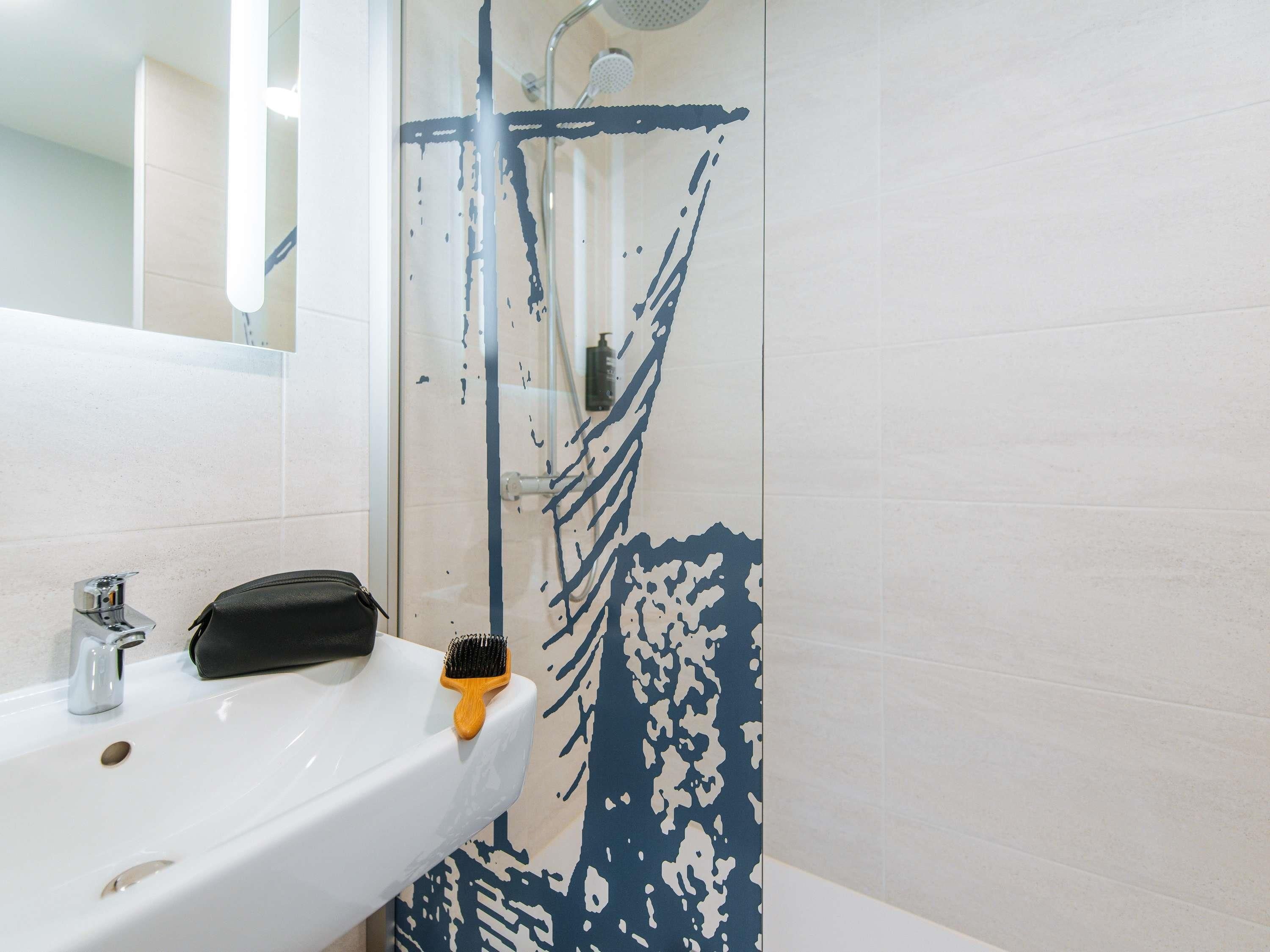 Une salle de bain avec un lavabo blanc, un miroir et une douche dont les murs sont décorés d’éclaboussures de peinture bleue.