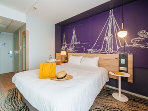 Una habitación de hotel con una cama, una mesita de noche, una lámpara, un muro con un mural náutico y una puerta.