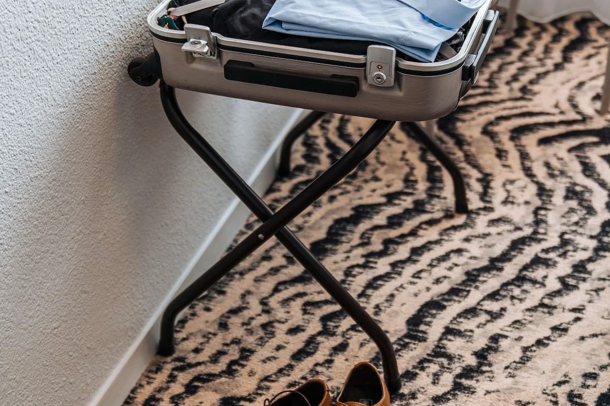 A suitcase on a metal stand against a wall, with a pair of shoes on the floor.