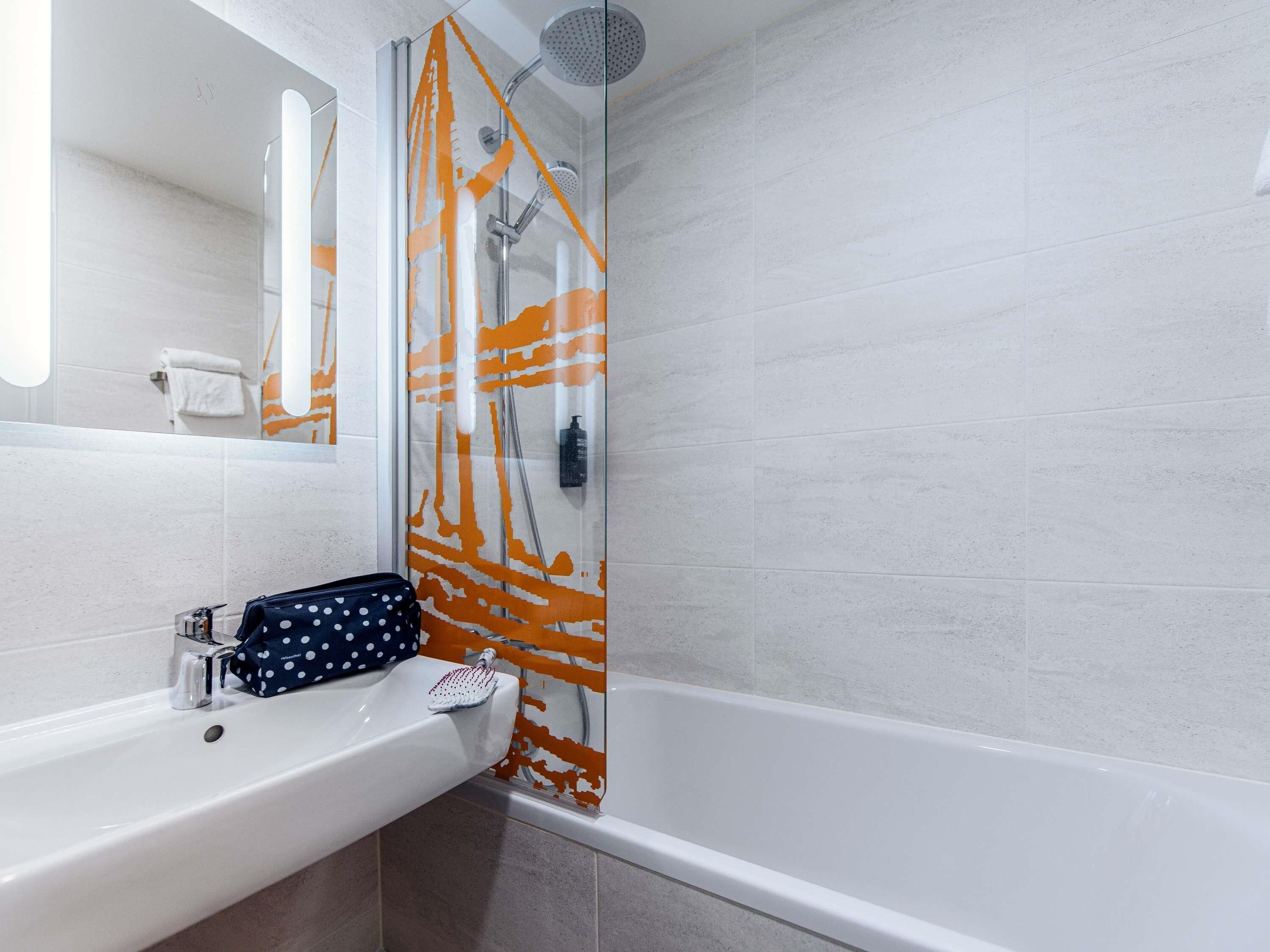 A bathroom with a white sink, a mirror, and a shower with an orange and white abstract design.