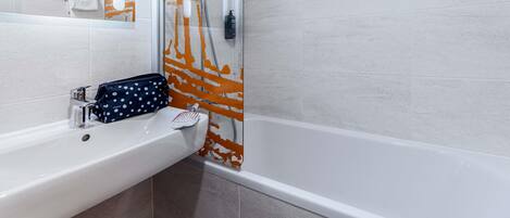 Un baño con un lavamanos blanco, un espejo y una ducha con un diseño abstracto en naranja y blanco.