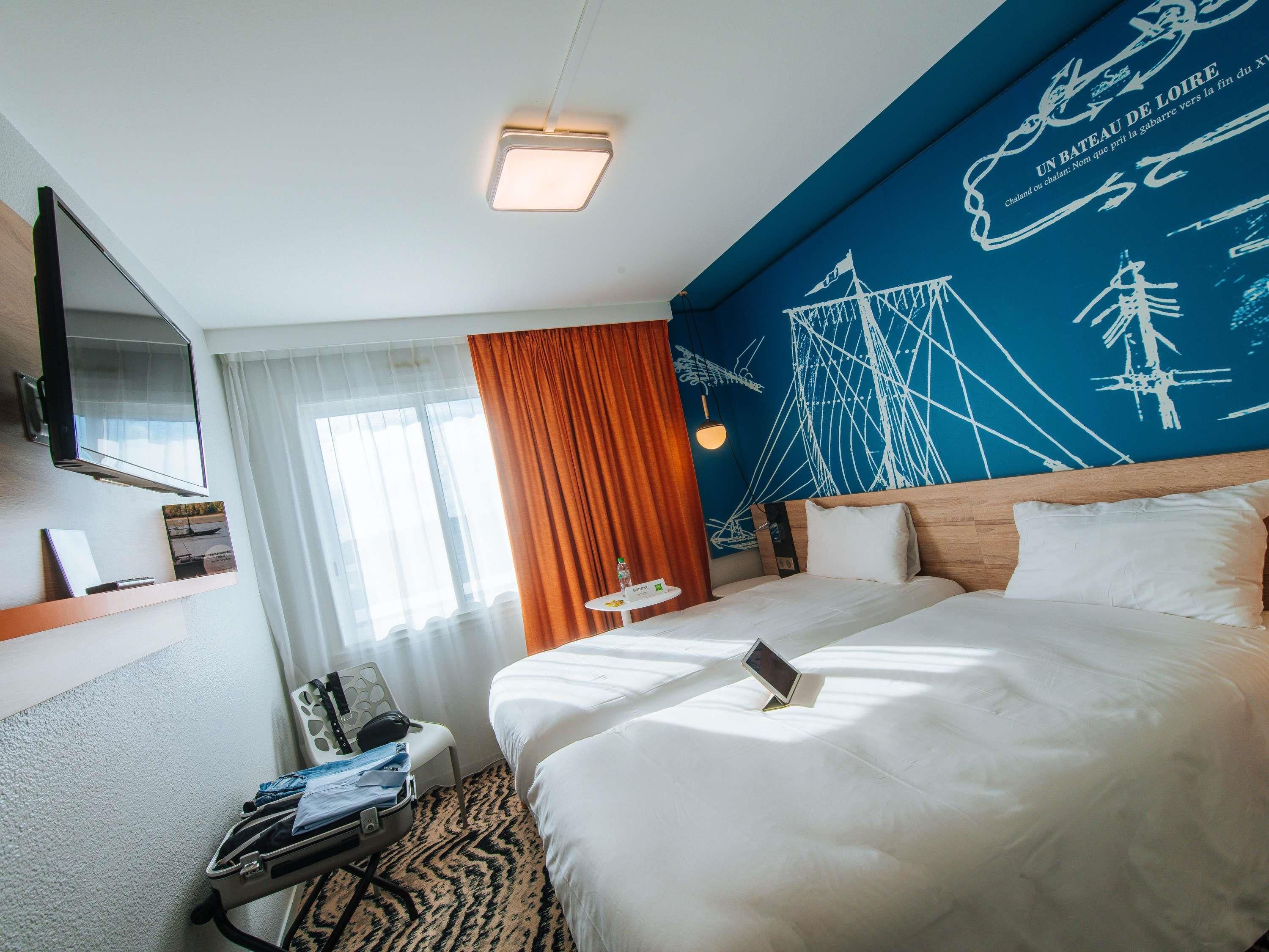 Een hotelkamer met een groot bed, een bureau met stoel, een flatscreen-tv en een muur met maritieme kunstwerken.