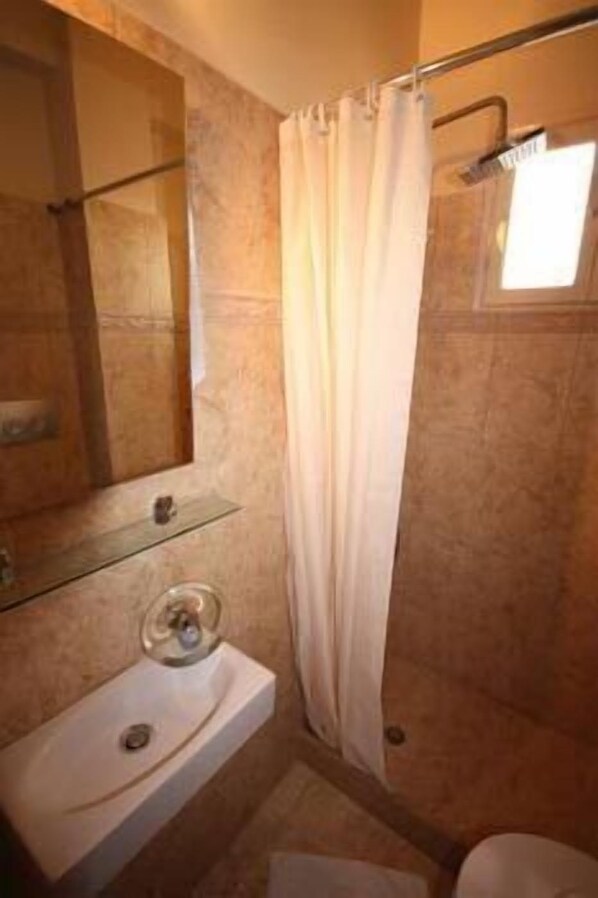 A bathroom with a glass shelf, a sink, and a shower curtain. - Hotel Plaza (Aegina)