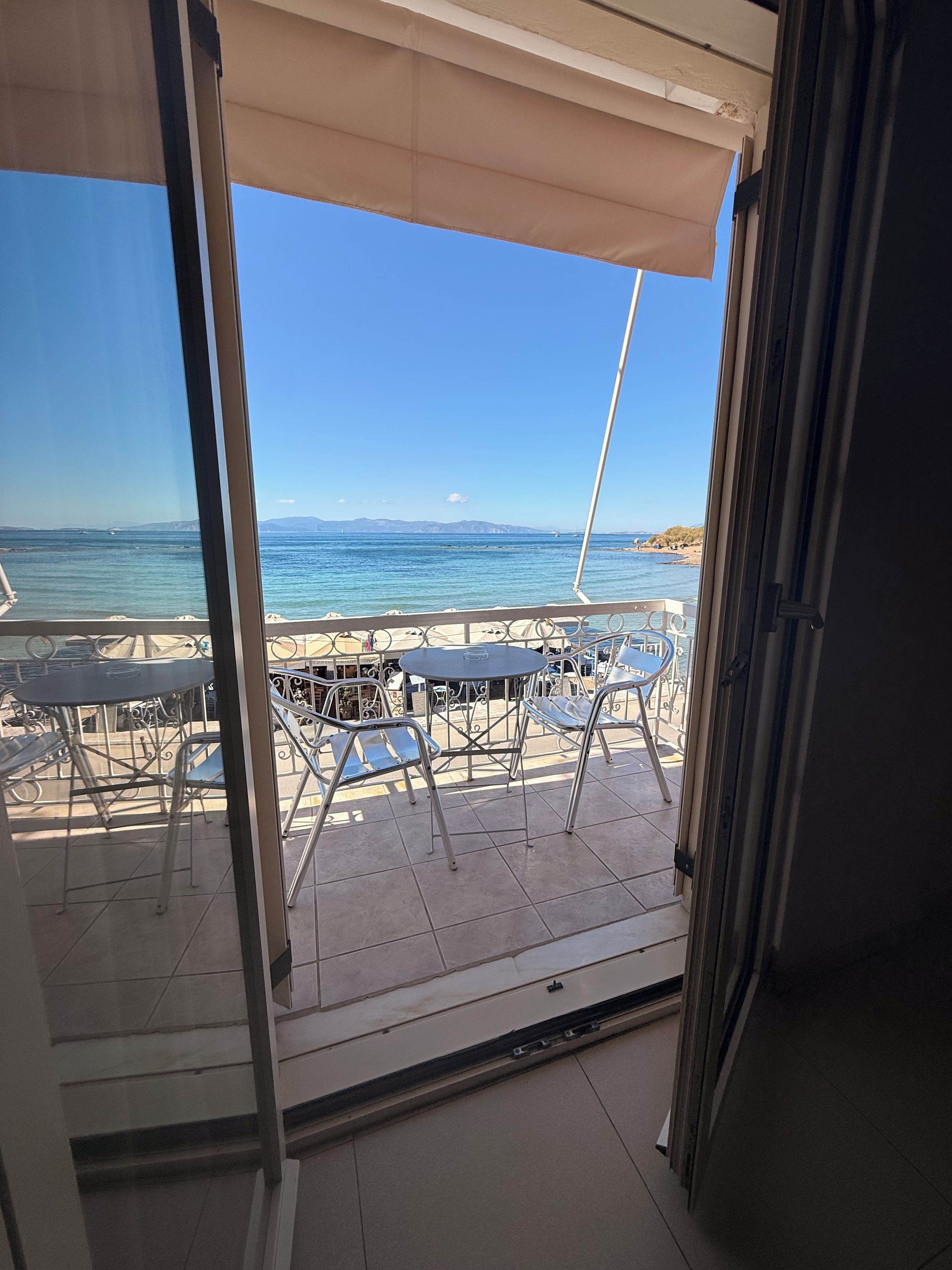 Una terraza con sillas y mesas de metal, con vista a una playa y al mar.