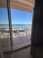 A terrace with metal chairs and tables, overlooking a beach and the sea.
