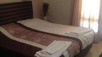 A neatly made bed with a brown headboard, a decorative pillow, and a folded white towel on the side.