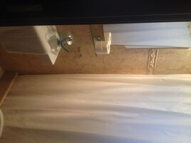 Un baño con cortina de ducha, toallero y soporte para papel higiénico en la pared.