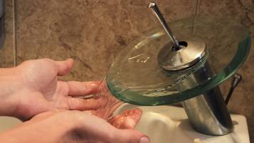 A hand under a glass water dispenser with a metallic spout.