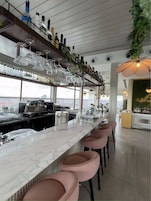Un'area bar con un bancone in marmo, sgabelli rosa e una selezione di bottiglie di liquore.