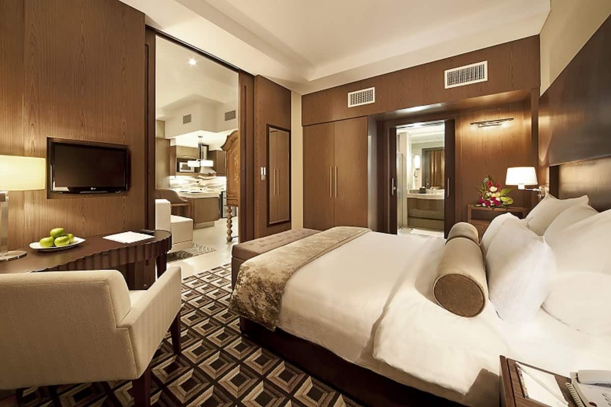 Habitación de hotel con una cama grande, un escritorio con televisor de pantalla plana, una silla y un rincón comedor con mesa y sillas.