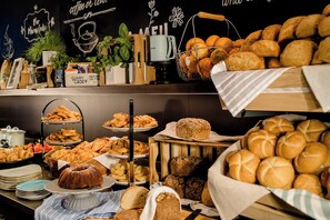 Buffet com diversos pães, doces e uma máquina de café.