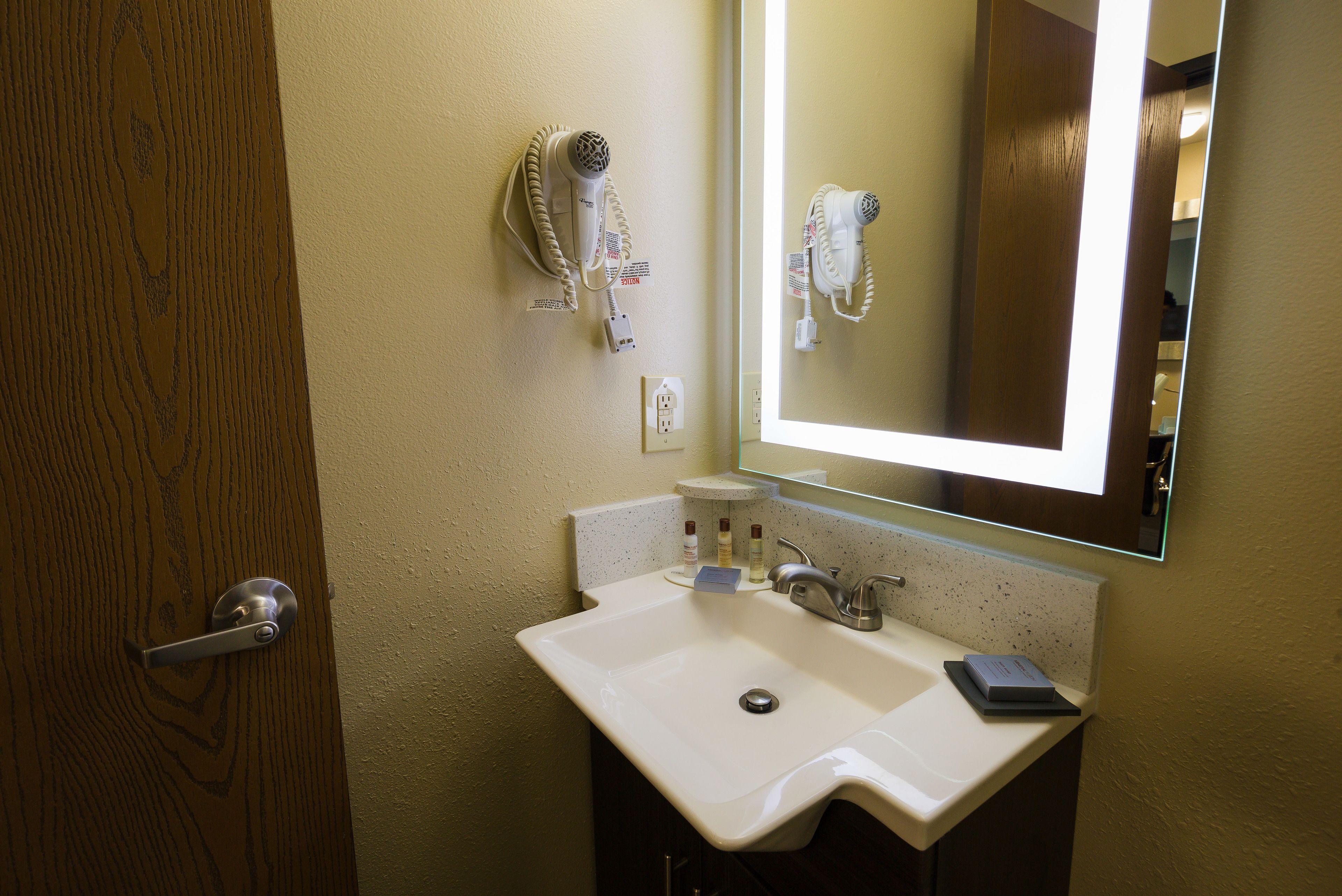 A bathroom with a white sink, a mirror, and a hairdryer mounted on the wall.