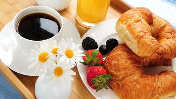 A breakfast tray with croissants, strawberries, blackberries, coffee, and a glass of orange juice.