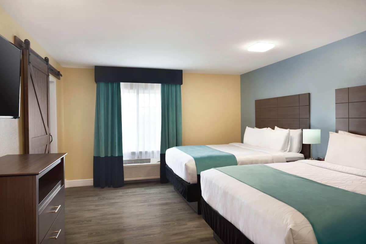 Quarto de hotel com duas camas, televisão, escrivaninha e janela com cortinas.