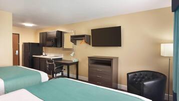 A hotel room with two beds, a kitchenette, a desk, a chair, and a wardrobe.